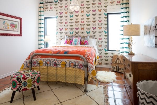 colorful quilt beddings, butterfly-designed wallpaper, decorative pillows, vintage lamp, vintage bedside table, antique bedframe, floral upholstered coffee table